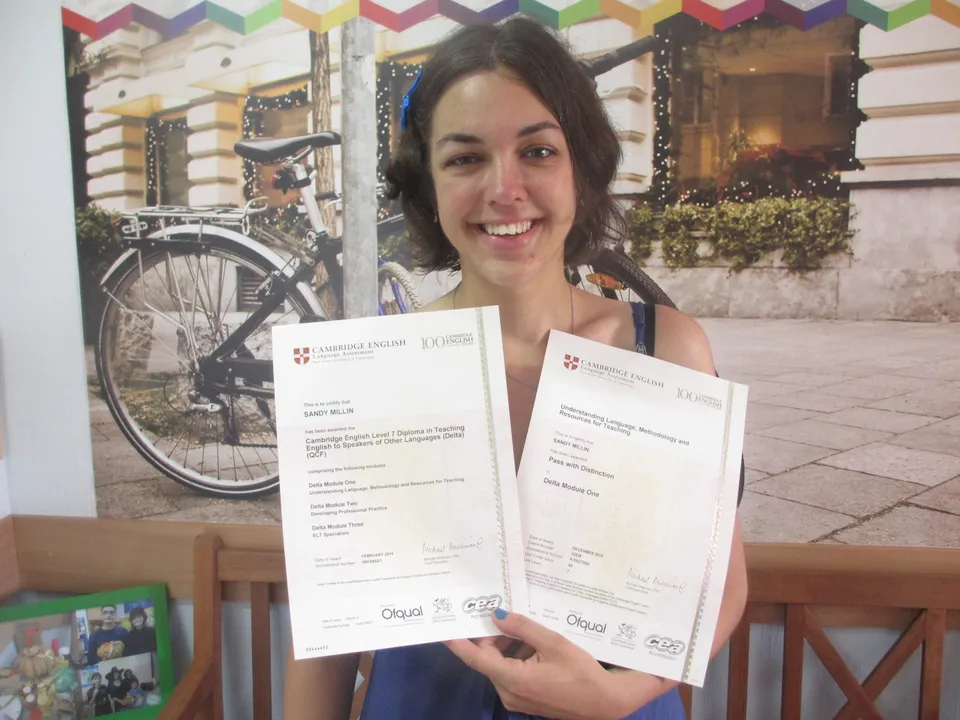 Sandy Millin smiling and holding her two Cambridge DELTA certificates